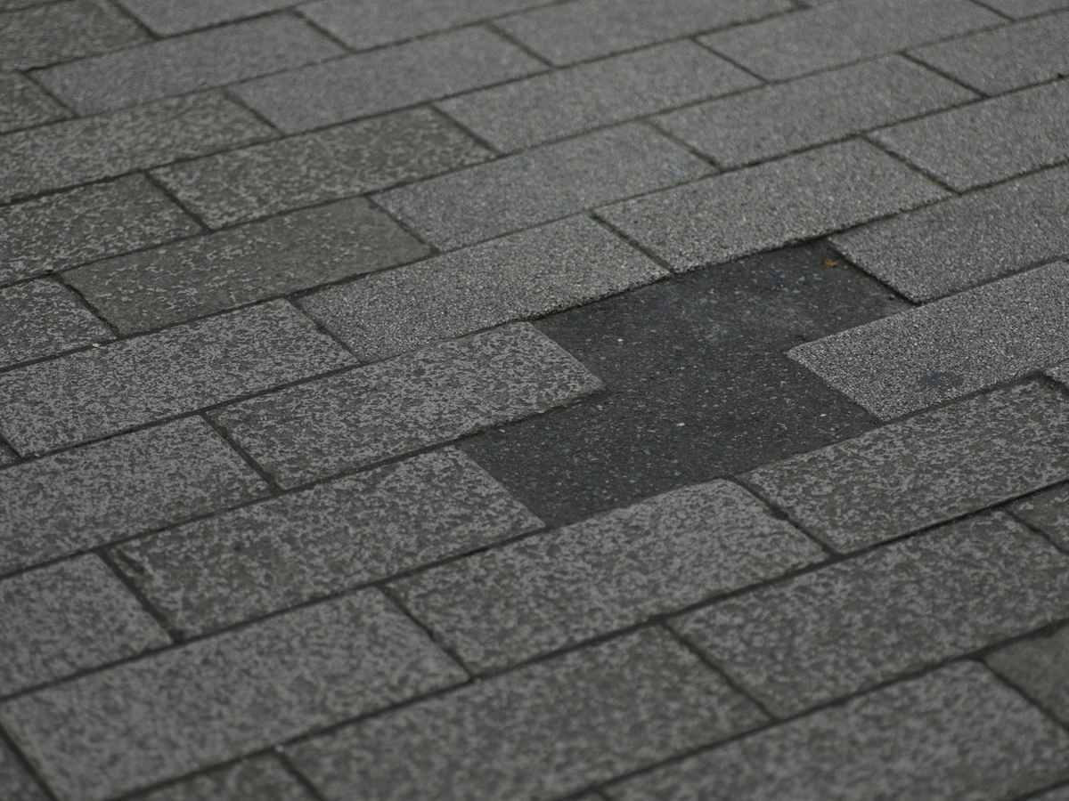A close-up of grey rectangular pavers with one patch of darker replacements in the middle